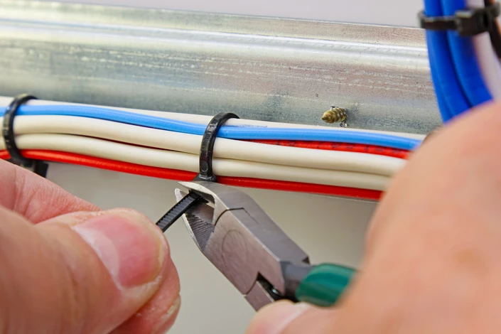 Scène d'atelier intérieur montrant des mains manipulant un outil de sertissage sur des câbles électriques