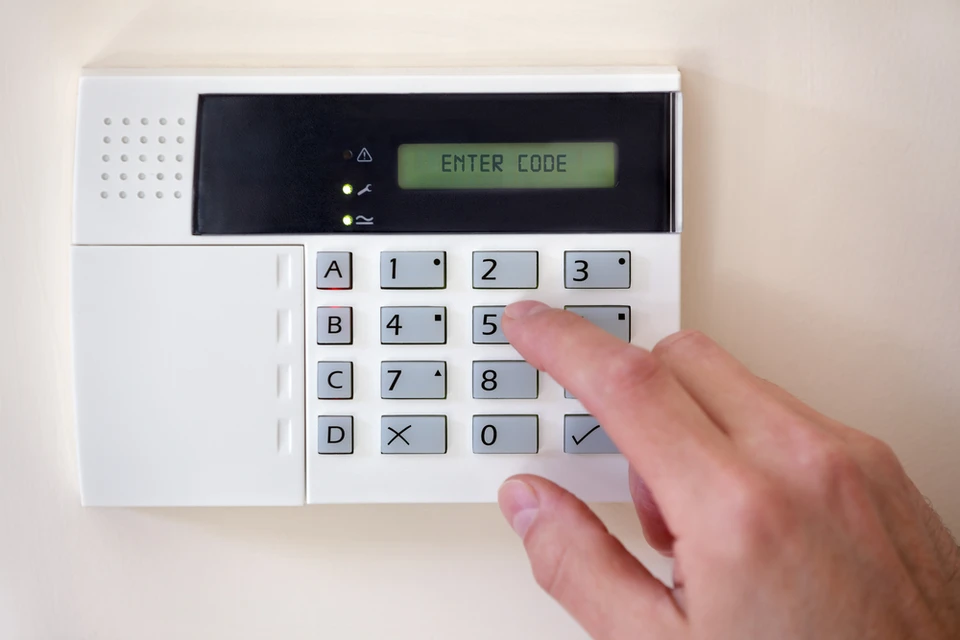 Main d'une personne tapant le code d'entrée sur un clavier de système d'alarme domestique mural