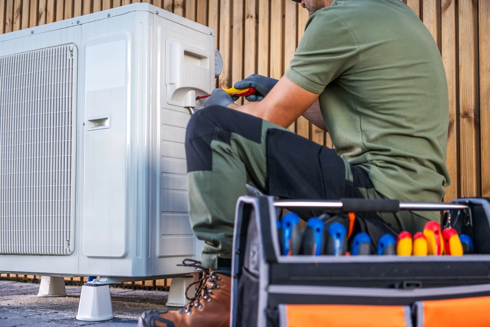 Un technicien travaille à l'entretien d'une unité de climatisation extérieure, à l'aide de divers outils et équipements dans un cadre résidentiel