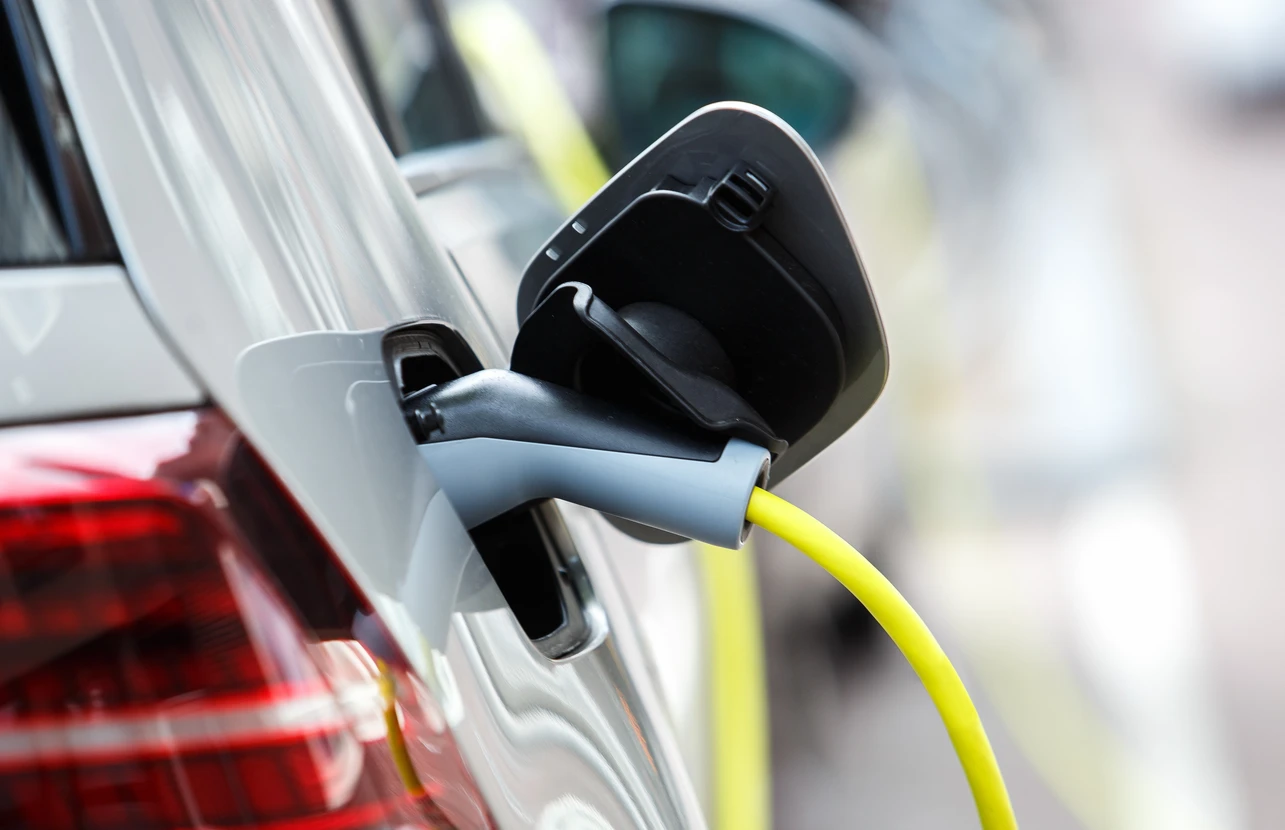 Scène extérieure avec véhicule électrique blanc en charge, câble d'alimentation jaune connecté au port de recharge latéral