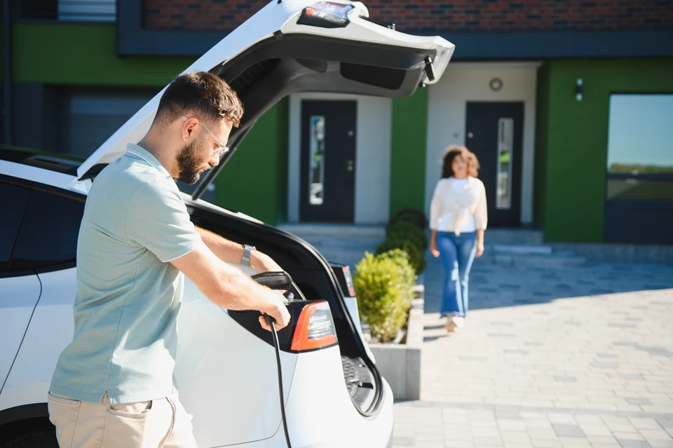 Scène extérieure urbaine avec véhicule électrique en charge sur voie pavée, environnement verdoyant avec arbres en arrière-plan, ambiance résidentielle calme
