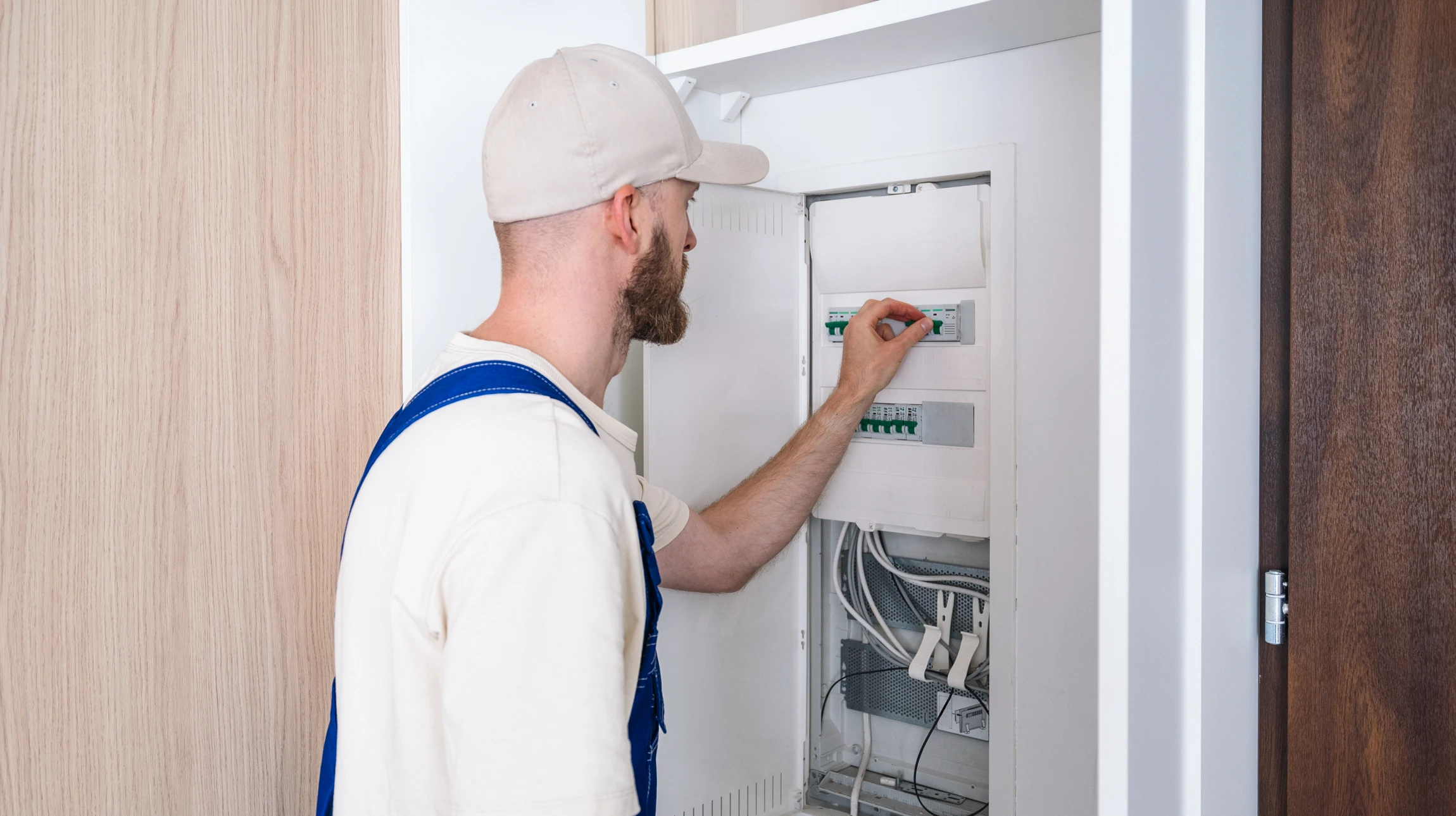 Électricien en tenue bleue effectuant des mesures électriques sur installation murale avec multimètre numérique orange