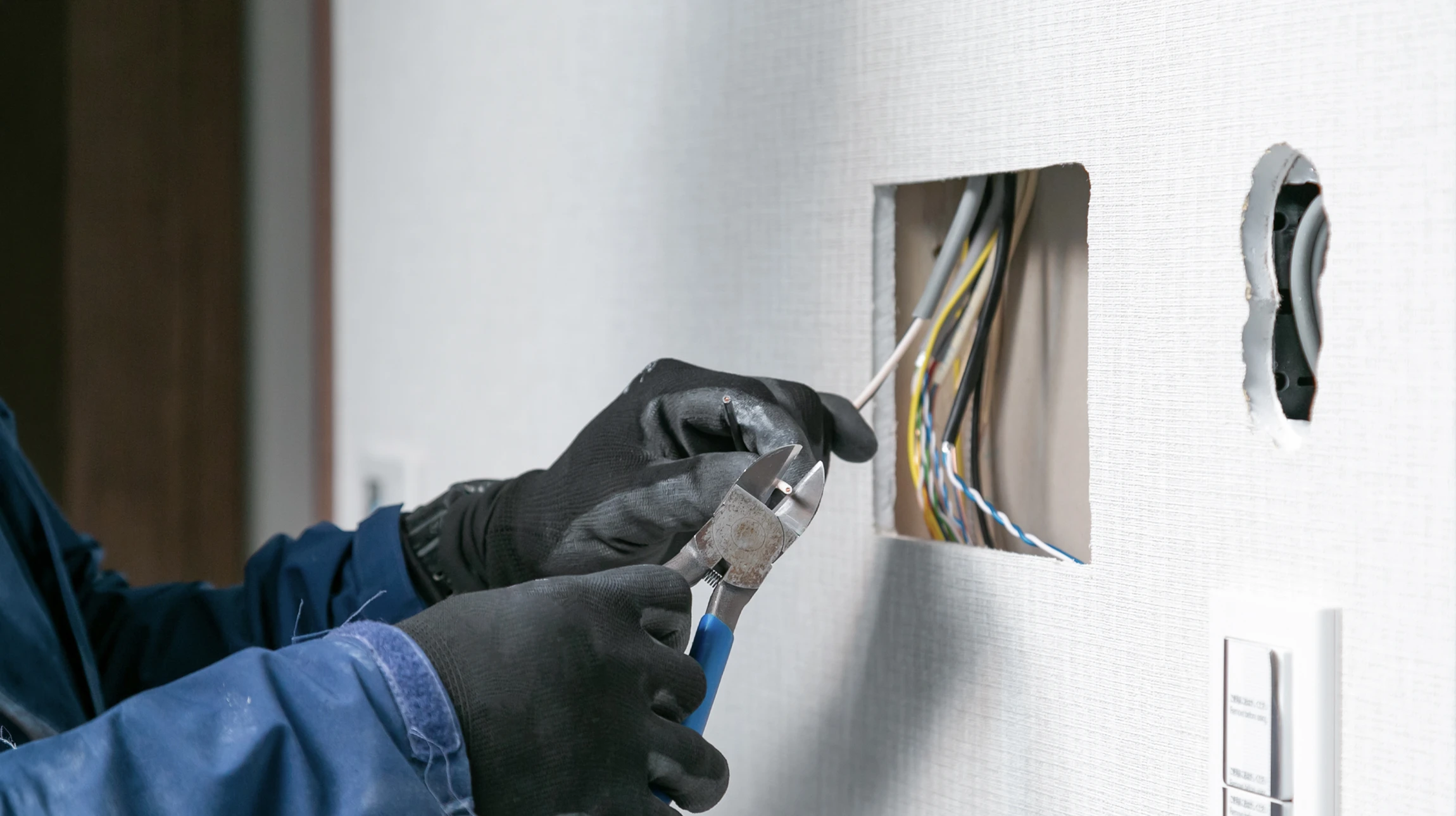 Électricien professionnel portant un casque de sécurité effectue des mesures électriques sur une prise murale résidentielle à l'aide d'un multimètre numérique